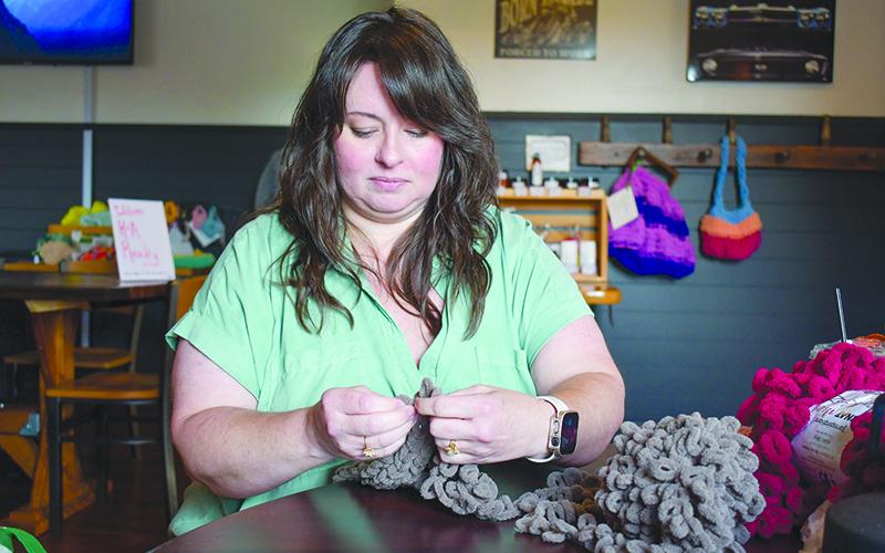Shannon Trotter knits a scarf using just her hands as she sits in BSG Coffee and Cafe. Some of her other creations hang on the wall behind her. JULIANNE AKERS/Staff 